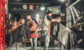 A bustling barbershop with two men getting haircuts, showcasing a vibrant barber environment.