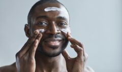 A cheerful African American man applying facial cream indoors.