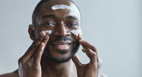 A cheerful African American man applying facial cream indoors.
