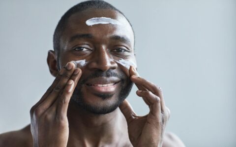 A cheerful African American man applying facial cream indoors.