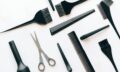 Flat lay of essential hairdressing tools including brushes, combs, and scissors on white background.