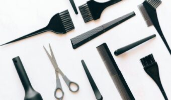 Flat lay of essential hairdressing tools including brushes, combs, and scissors on white background.