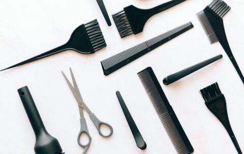 Flat lay of essential hairdressing tools including brushes, combs, and scissors on white background.