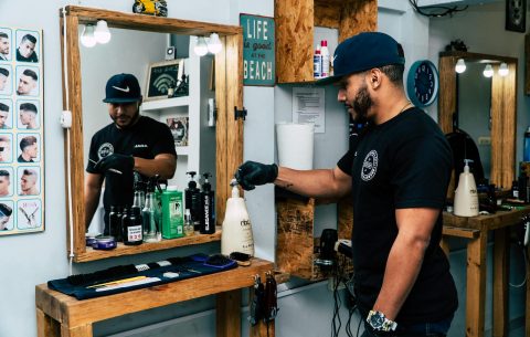 A barber in a stylish shop preparing tools for a haircut. Modern interior design with mirrors and grooming products.