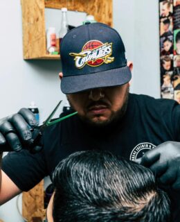 Barber wearing a cap and gloves styles a man's hair in a barbershop.
