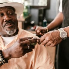 Photo by RDNE Stock project Senior man with a hat giving a tip to a young barber indoors, wearing bracelets and a watch.