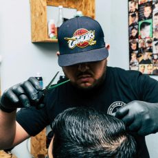Photo by Jose Ricardo Barraza Morachis Barber wearing a cap and gloves styles a man's hair in a barbershop.